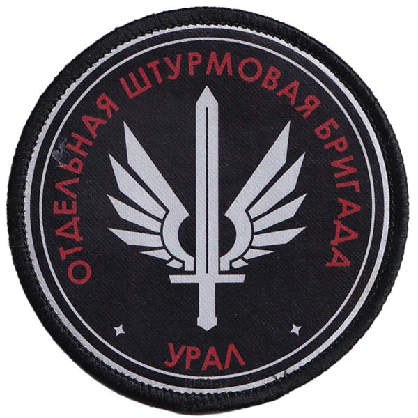 Ural Assault Brigade Patch with red Cyrillic unit lettering, silver winged sword emblem, black circular field, and modern Russia–Ukraine conflict context.