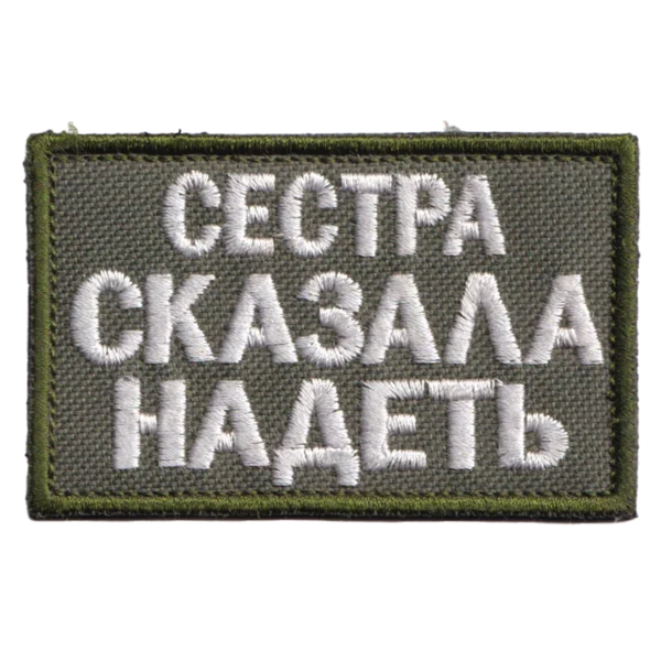 Russian Sister Told Me Patch with white Cyrillic text embroidered on olive fabric, green border, and hook-and-loop backing.